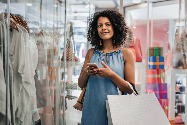 Smiling woman using her cellphone while out clothes shopping - Foto, Imagen