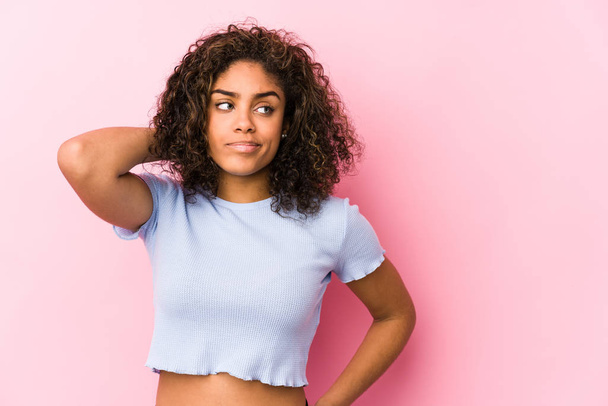 Giovane donna afroamericana su uno sfondo rosa che tocca la nuca, pensando e facendo una scelta
. - Foto, immagini