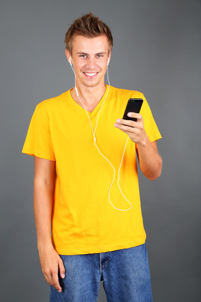 Handsome young man listening to music on grey background - Photo, image