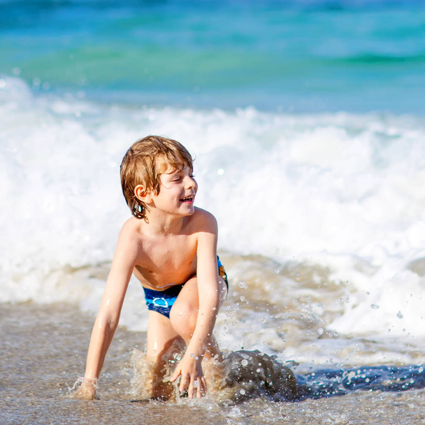 entzückender kleiner blonder Junge, der Spaß am Strand hat. aufgeregtes Kind spielt mit Wellen, schwimmt, plantscht und freut sich über Familienurlaub in Miami, Florida, USA - Foto, Bild