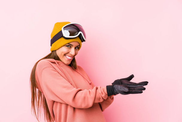 Νεαρή Καυκάσια γυναίκα που φοράει ρούχα του σκι απομονωμένη κρατώντας ένα αντίγραφο χώρου σε μια παλάμη. - Φωτογραφία, εικόνα