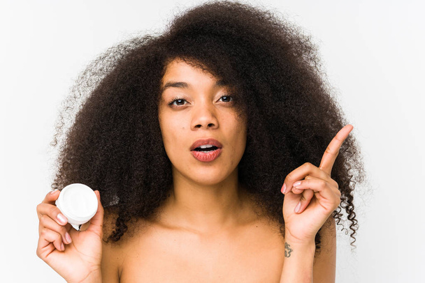 Jeune femme afro tenant une crème hydratante isolée ayant une bonne idée, concept de créativité
. - Photo, image