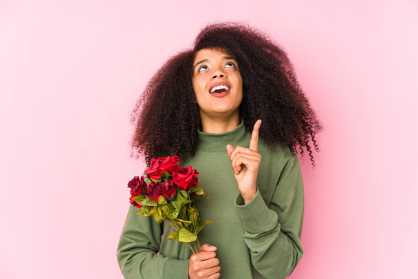 Joven mujer afro sosteniendo una rosa aislada Joven mujer afro sosteniendo una rosa apuntando al revés con la boca abierta
. - Foto, Imagen