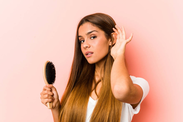 Joven mujer caucásica sosteniendo un cepillo de pelo tratando de escuchar un chisme
. - Foto, Imagen