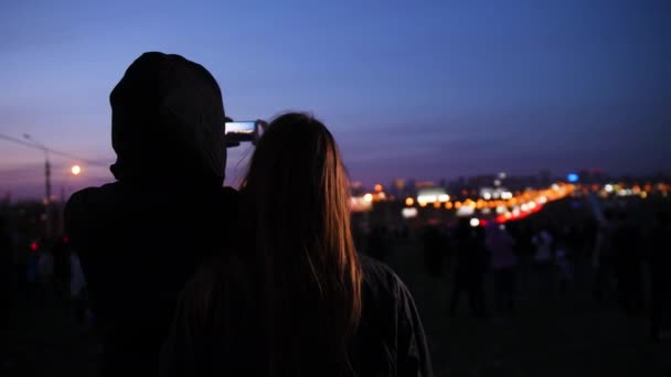 Um cara e uma menina olham para a visão noturna da cidade e tiram fotos
 - Filmagem, Vídeo