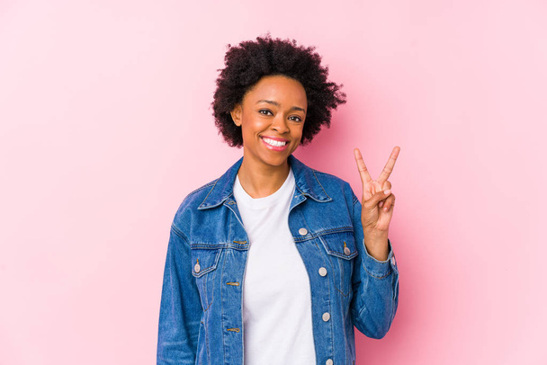 Mujer afroamericana joven contra un fondo rosa aislado mostrando signo de victoria y sonriendo ampliamente
. - Foto, Imagen