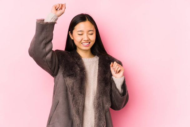 Νεαρή Κινέζα που φοράει παλτό απομονωμένη γιορτάζοντας μια ξεχωριστή μέρα, πηδάει και σηκώνει τα χέρια με ενέργεια.. - Φωτογραφία, εικόνα