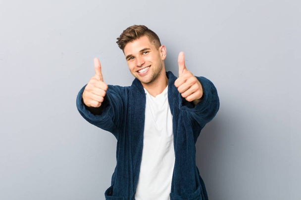Fiatal fehér férfi visel pizsamát hüvelykujjal felfelé, éljenzés valami, támogatás és tisztelet koncepció. - Fotó, kép