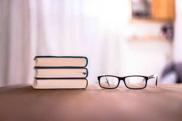 Stack of books and glasses lying on wooden desk at home. Knowledge and science - 写真・画像