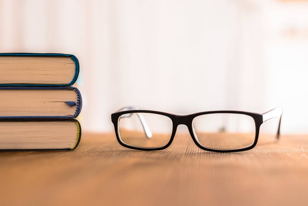 Stack of books and glasses lying on wooden desk at home. Knowledge and science - Fotoğraf, Görsel