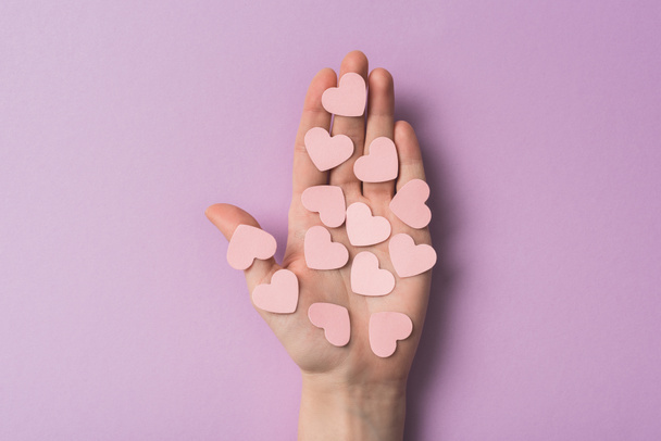 cropped view of woman holding pink paper hearts on violet background - Photo, Image