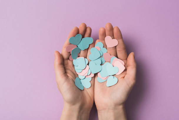 cropped view of woman holding colorful paper hearts on violet background - Fotoğraf, Görsel