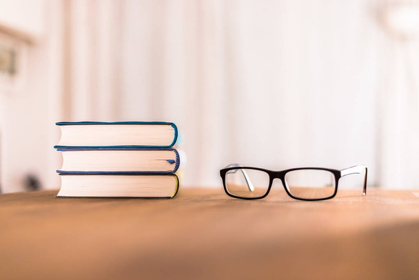 Stack of books and glasses lying on wooden desk at home. Knowledge and science - Foto, afbeelding