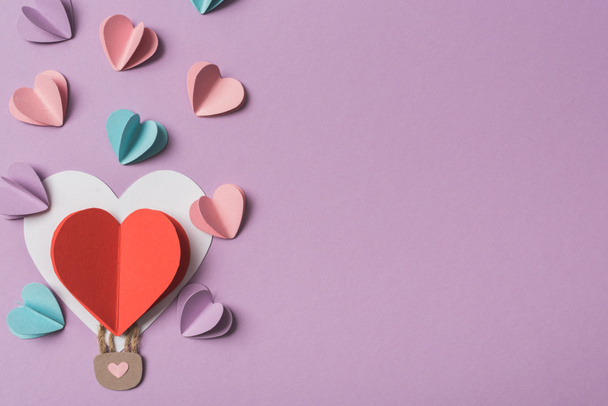 horní pohled na barevné papírové srdce kolem srdce ve tvaru papírového balónu vzduchu na fialovém pozadí - Fotografie, Obrázek