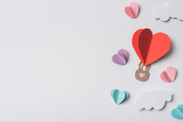 top view of colorful paper hearts and air balloon with clouds on white background - Fotografie, Obrázek
