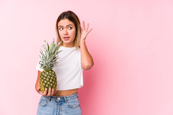 Young caucasian woman holding a pineapple trying to listening a gossip. - Photo, Image