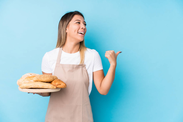 Young caucasian baker woman isolated points with thumb finger away, laughing and carefree. - Foto, Imagem