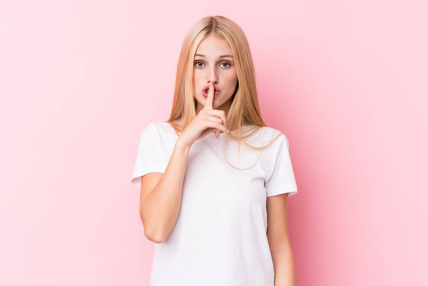 Young blonde woman on pink background keeping a secret or asking for silence. - Photo, Image