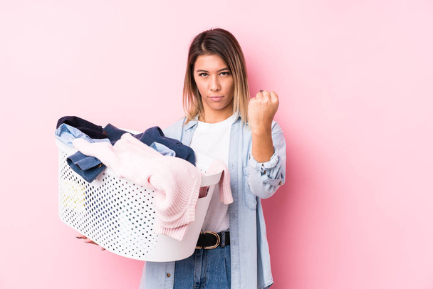 Young caucasian woman picking up a dirty clothes showing fist to camera, aggressive facial expression. - Фото, изображение