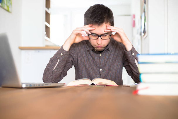 Мужской выхлоп и несчастный студент исследует и учится дома, стопка книг размыта
 - Фото, изображение