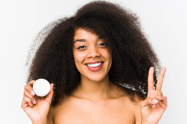 Jeune femme afro tenant une crème hydratante isolée montrant numéro deux avec les doigts
. - Photo, image