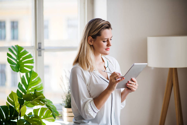 Young woman with tablet indoors in home office, working. - Foto, Bild