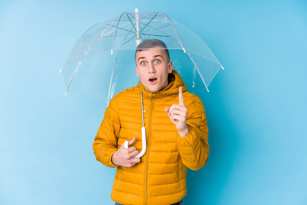Young caucasian man holding an umbrella having an idea, inspiration concept. - Photo, Image