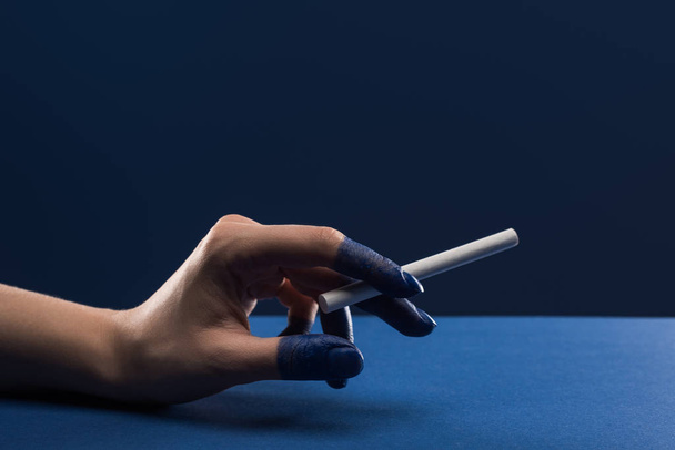 cropped view of female hand with painted fingers holding cigarette isolated on blue - Photo, image