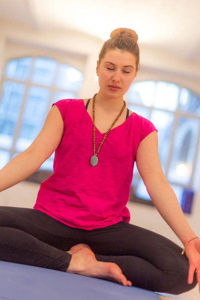 Młoda kobieta siedząca ze skrzyżowanymi nogami ćwicząca jogę na macie demonstrującej pozycję lotosu, pozycję do jogi asany - Zdjęcie, obraz