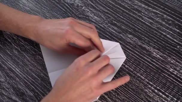 Assembling a white paper origami plane on a black textural wooden table with the hands of a young man - Кадри, відео