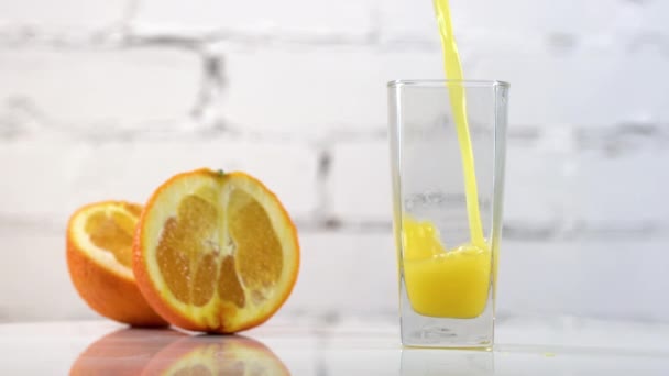 Jugo de naranja recién exprimido vertiendo en un vaso sobre una mesa con rodajas de naranjas al lado. Refrescante bebida amarilla con frutas sobre fondo blanco
 - Imágenes, Vídeo