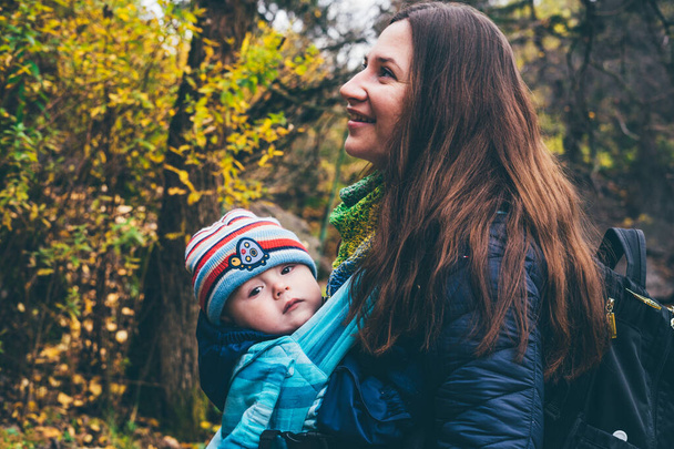 Mother with her baby in a sling scarf is standing in a botanical garden. - Photo, Image