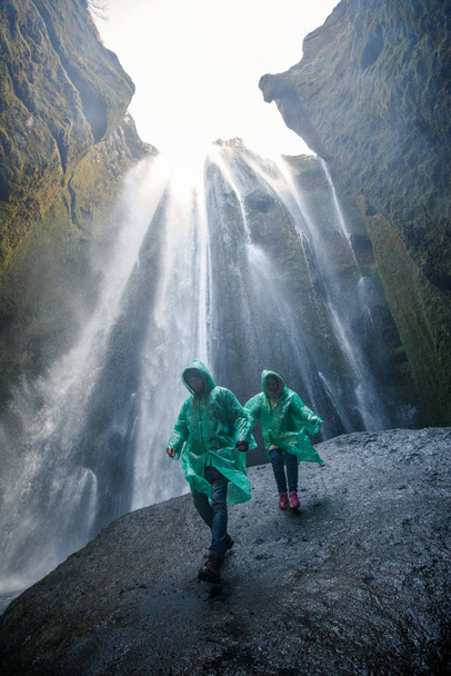 couple in green raincoats walking near waterfall in iceland mountains - Foto, Imagen