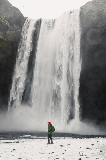 jóképű fiatalember áll vízesés mellett Izlandon hegyek háttér  - Fotó, kép