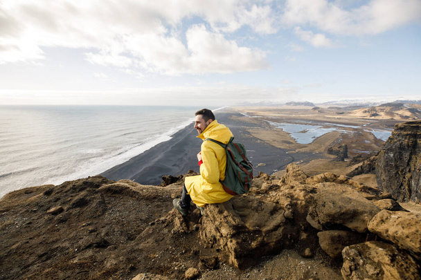 inviting young man on cliff with black sand beach on Iceland mountains view background - Foto, Bild