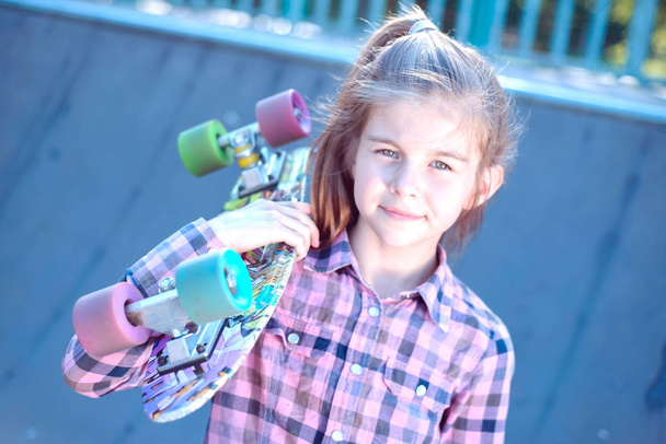 Πορτρέτο ενός όμορφου μικρού κοριτσιού που κρατά ένα skateboard στον ώμο της - Φωτογραφία, εικόνα
