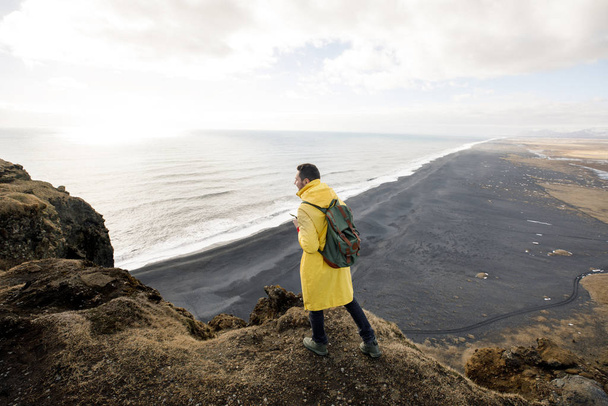 inviting young man on cliff with black sand beach on Iceland mountains view background - Foto, Imagem