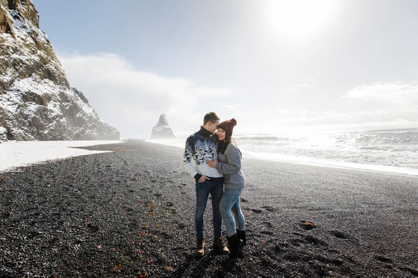 romantic and happy couple walking on black sand Iceland beach in Norwegian sea - Fotó, kép
