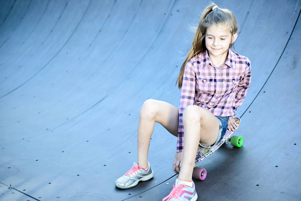 μικρό κορίτσι κάθεται σε ένα skateboard, skatepark στο δρόμο - Φωτογραφία, εικόνα