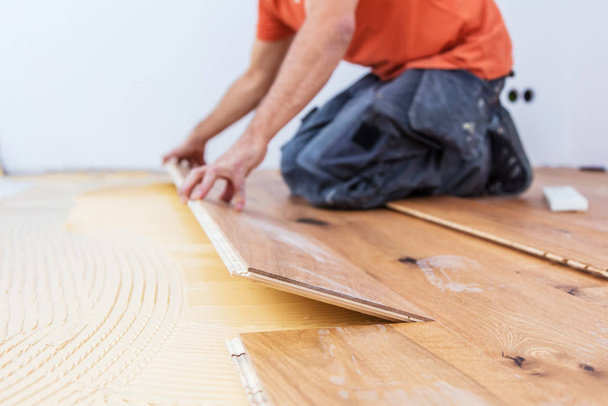 建設現場に寄木細工の床を設置する男性労働者の切り取られたショット。寄木細工の床    - 写真・画像