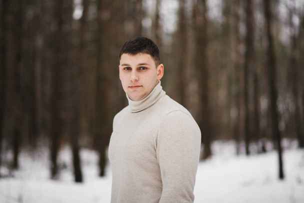 Portrait of a stylish young man on the background of a snowy forest - Fotó, kép