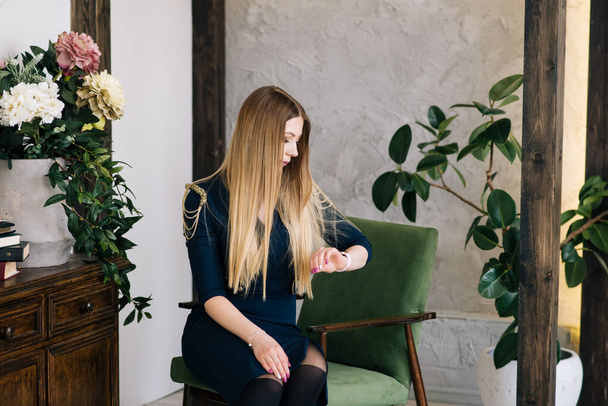 Portrait of a beautiful young stylish businesswoman in an interior Studio. The girl looks at the smart watch - Фото, зображення