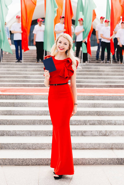 Beautiful young blonde smiling getting a diploma of education. Graduate in a red dress with a diploma - 写真・画像