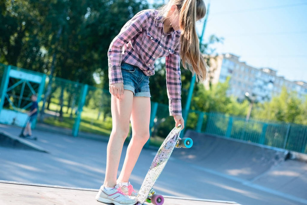 portrait of a little teenage girl, holding in hand skateboard, trains to do the trick - Foto, imagen