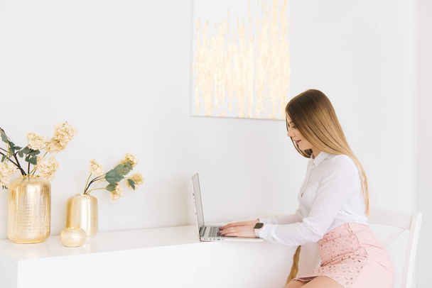Portrait of a beautiful young businesswoman in a skirt and blouse with a laptop on a white background in a modern interior - 写真・画像