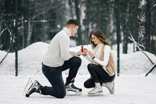 Winter love story on ice. The guy offers to marry a girl standing on his knee in the hands of a wedding ring on the ice on the skates - Φωτογραφία, εικόνα