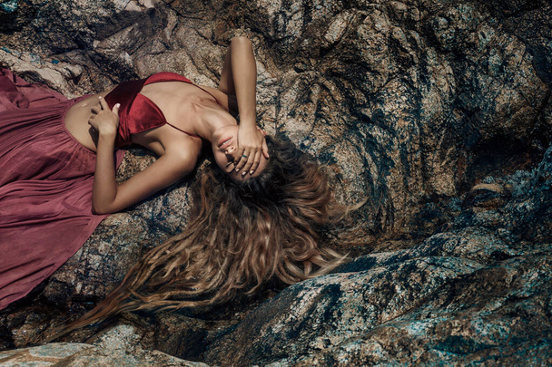 young attractive woman lying on rocks on sea beach - 写真・画像