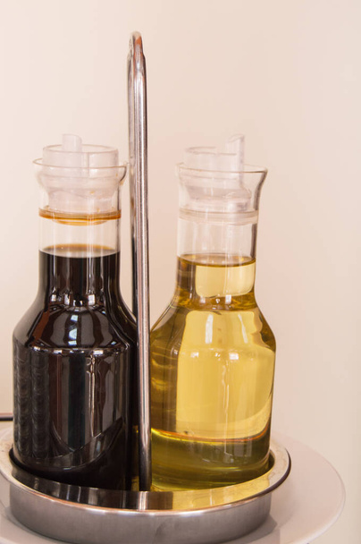 Комплект бальзамического уксуса или соевого соуса и оливкового масла в стеклянных бутылках на столе в кафе или ресторане, вертикальный кадр
 - Фото, изображение