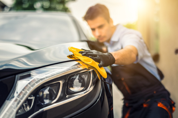Car detailing - the man holds the microfiber in hand and polishes the car. Selective focus. - Zdjęcie, obraz