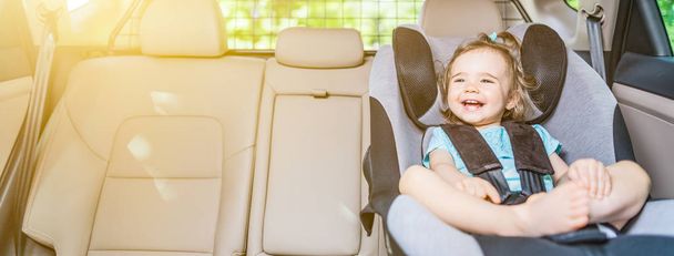Hermosa niña sonriente abrochada con cinturón de seguridad en asiento de seguridad
 - Foto, imagen